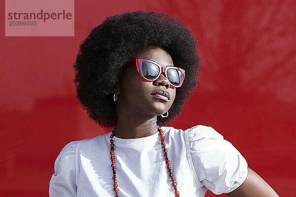 Confident young woman with Afro hairstyle wearing sunglasses in front of red window