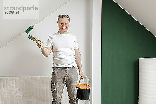 Smiling man holding paint can and roller at home