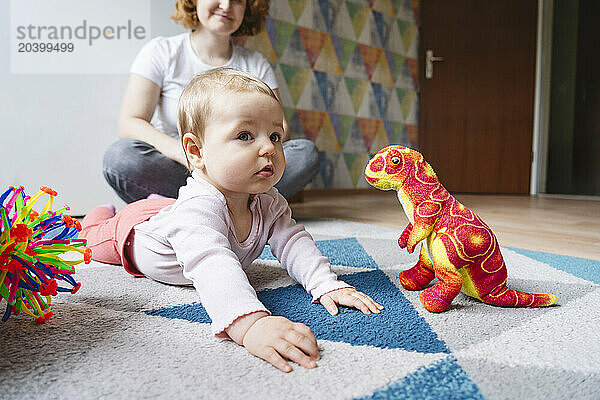 Girl lying next to dinosaur plush toy at home