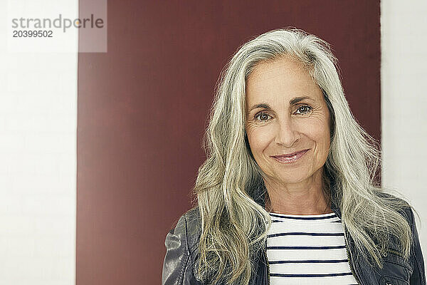 Smiling woman with gray hair against maroon background