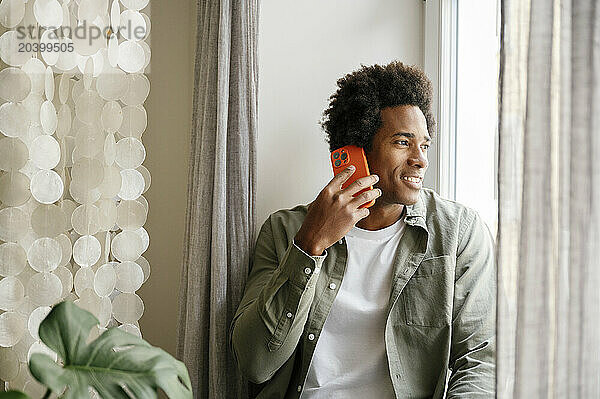 Smiling man talking on mobile phone sitting by hanging decor at home