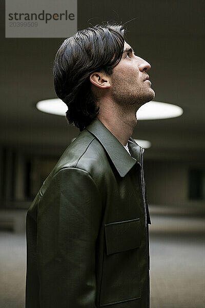 Young man wearing green leather jacket looking up in illuminated parking garage