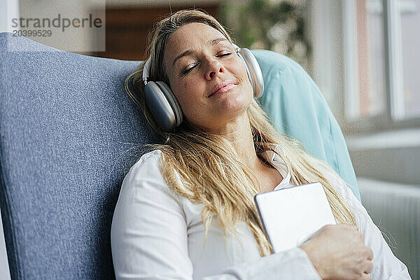 Businesswoman with wireless headphones and tablet PC relaxing on chair at office