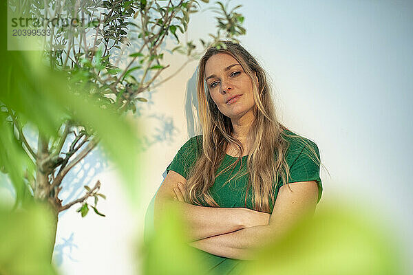 Confident businesswoman standing with arms crossed by plants