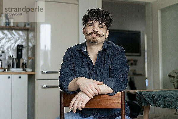 Man with mustache sitting on chair in kitchen at home