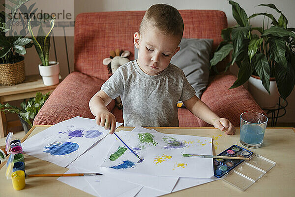 Boy painting on sheet of paper using brush at home