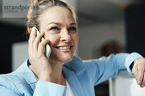 Smiling mature businesswoman talking through smart phone in office