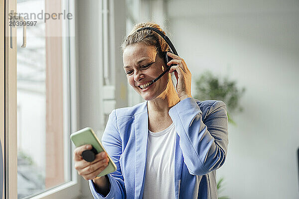 Happy businesswoman talking through headset using mobile phone in office