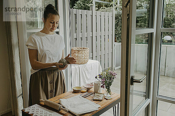 Woman molding clay standing by table at home