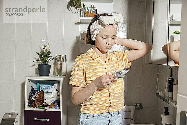 Girl reading instruction on beauty package in bathroom