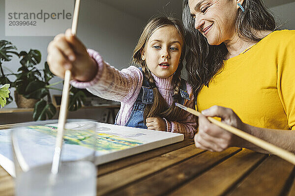 Grandmother and granddaughter painting together at table at home