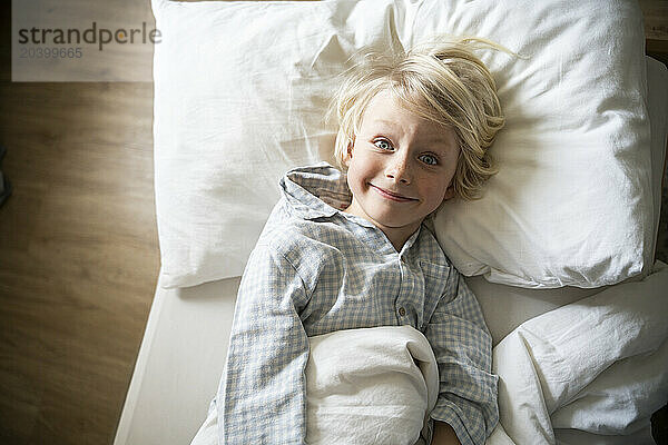 Smiling boy wearing pajamas and lying on bed at home