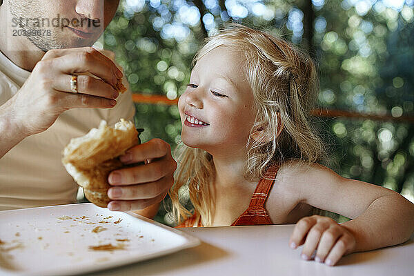 Father and daughter eating croissant together at home