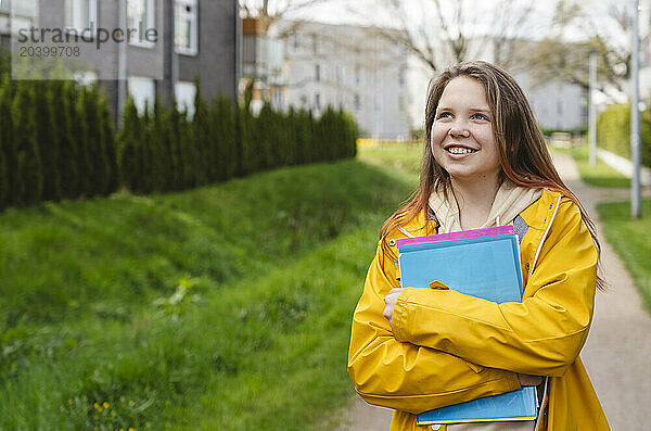 Smiling girl holding folders and standing on footpath