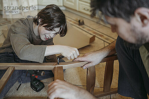 Son helping father in repairing wooden chair at home