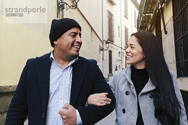 Happy couple walking with arms around amidst buildings