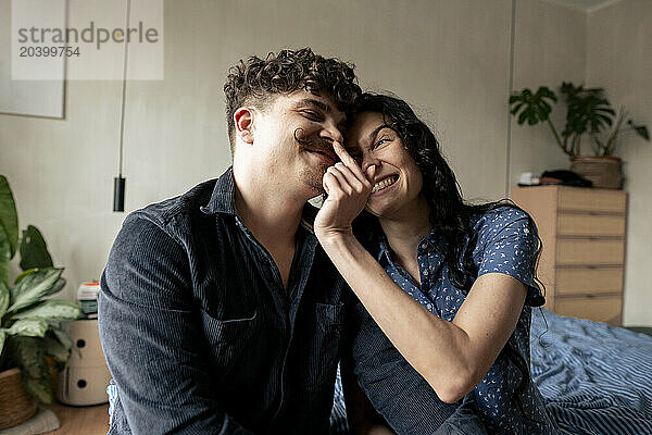 Smiling woman touching nose of boyfriend at home