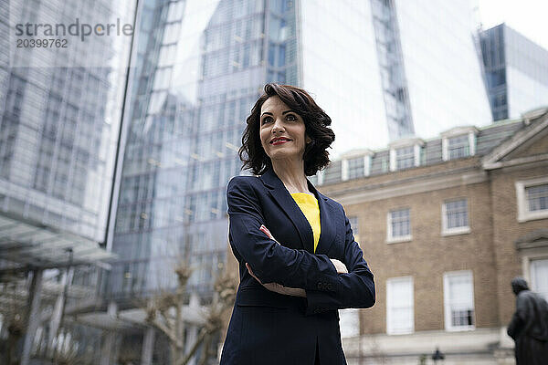 Smiling businesswoman in blazer standing with arms crossed