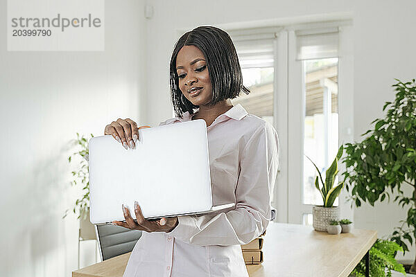 Businesswoman holding laptop standing at office