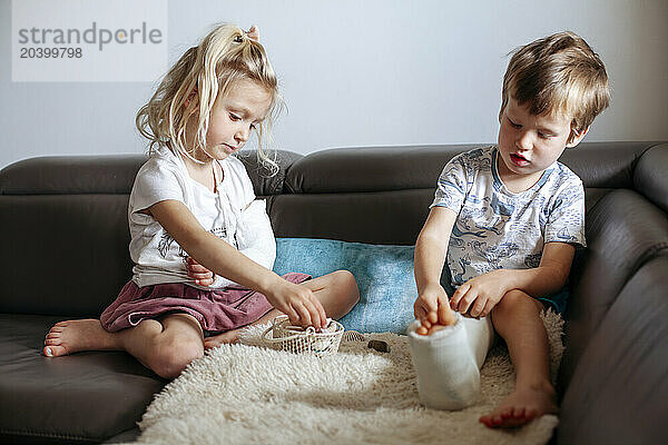 Siblings with broken leg and arm sitting on sofa at home