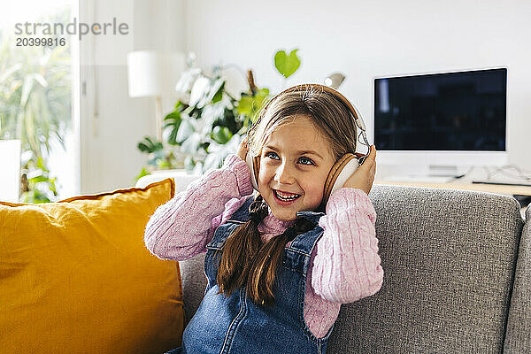 Happy girl listening to music through wireless headphones at home