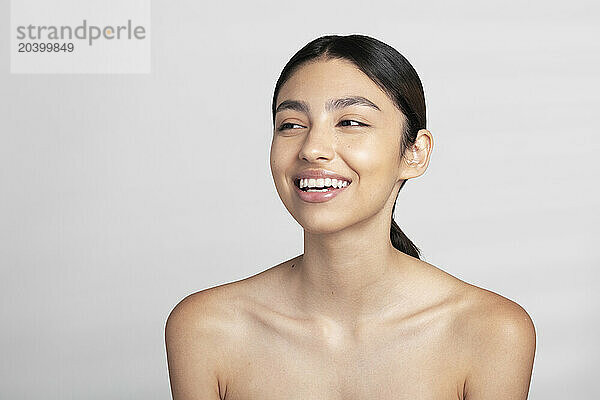 Happy beautiful young naked woman looking away against white background