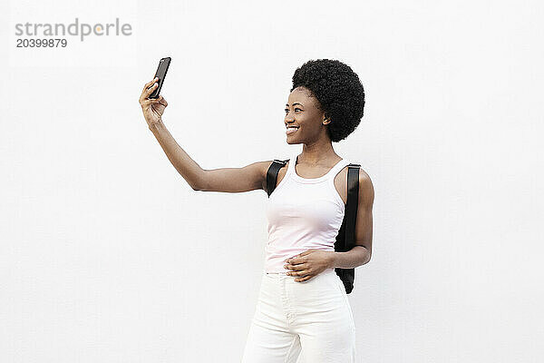 Smiling woman taking selfie through smart phone against white background