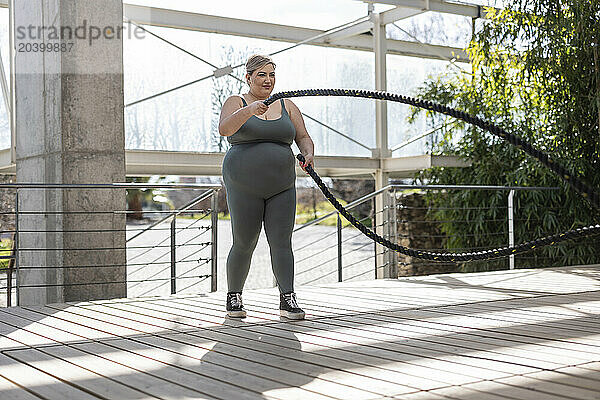 Curvy woman exercising with rope on footbridge at park