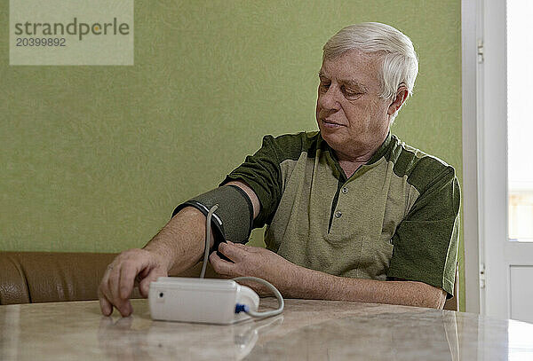 Elderly man wearing blood pressure gauge sitting at home