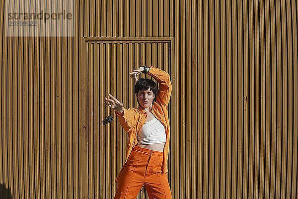 Confident woman wearing orange casuals dancing in front of brown wall