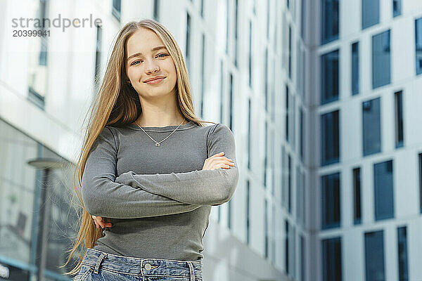 Confident teenager with arms crossed in front of building