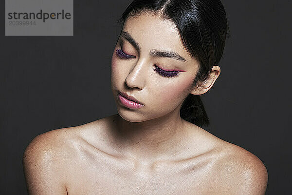 Beautiful young woman with make-up on face against grey background