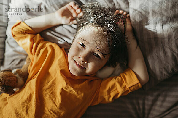 Portrait of a cute boy with long hair lying on bed in orange sweatshirt at home