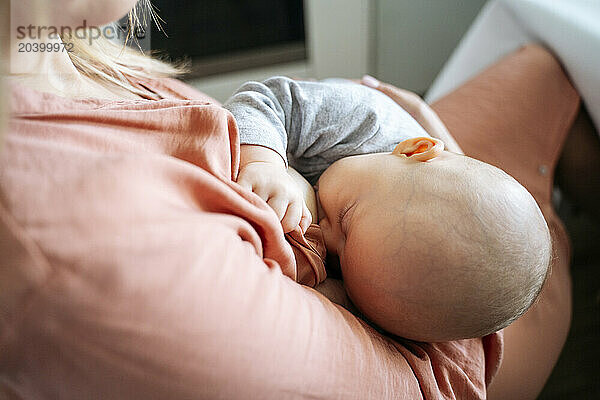 Mother breastfeeding baby boy sitting in kitchen