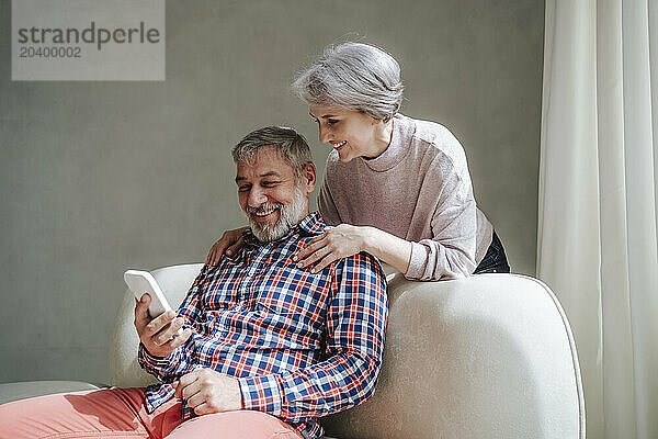 Mature woman leaning on man video calling through smart phone at home