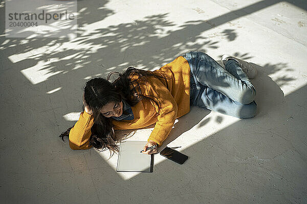 Young woman using tablet PC lying on floor at home