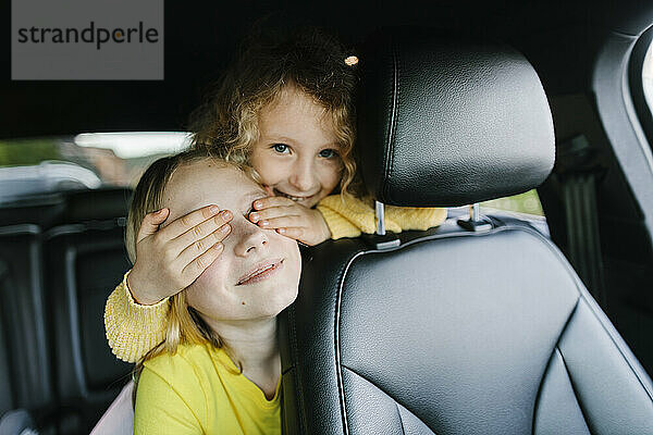 Girl covering eyes of sister in car