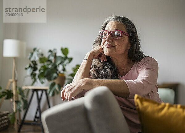 Thoughtful mature woman with eyeglasses sitting on sofa in living room at home