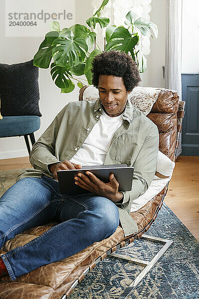 Smiling businessman using laptop reclining on lounge chair working at home