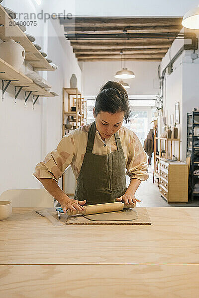 Skilled artist rolling out clay on table in pottery studio