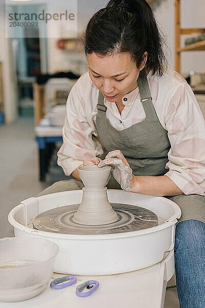 Confident artist molding clay on pottery wheel at art workplace