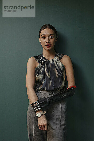 Confident young woman with black bionic arm leaning on green wall