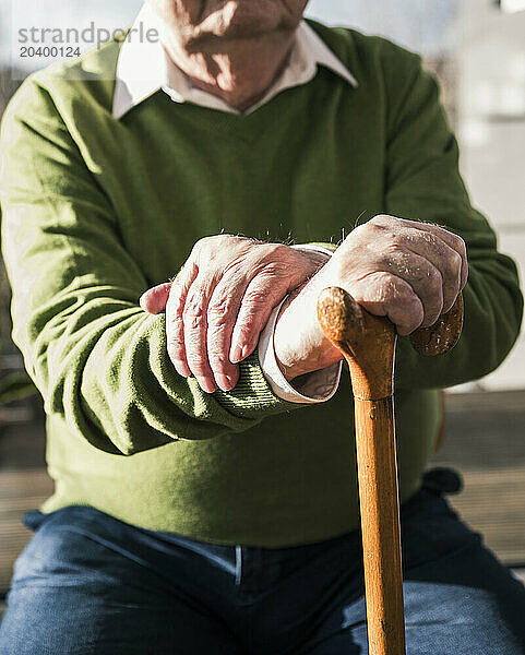 Senior man sitting with walking cane under sunlight