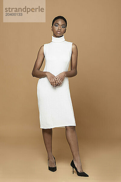 Fashion model wearing white dress standing against beige background