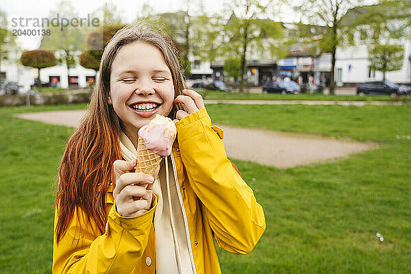 Happy girl wearing yellow raincoat and having ice cream at park