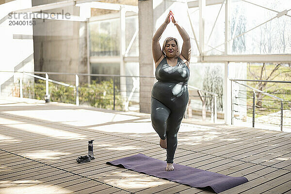 Curvy woman practicing tree pose on mat in park