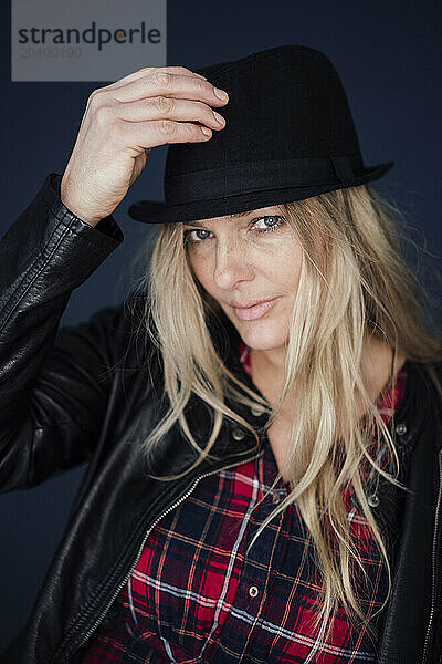 Blond mature woman wearing hat and jacket against colored background