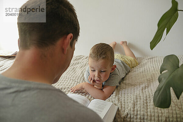 Son listening to father reading book at home