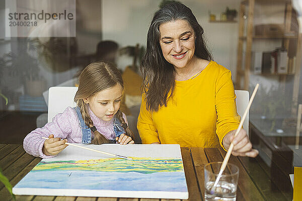 Grandmother and granddaughter painting together seen through window