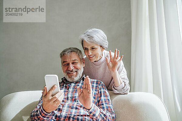 Smiling mature couple waving on video call through smart phone at home